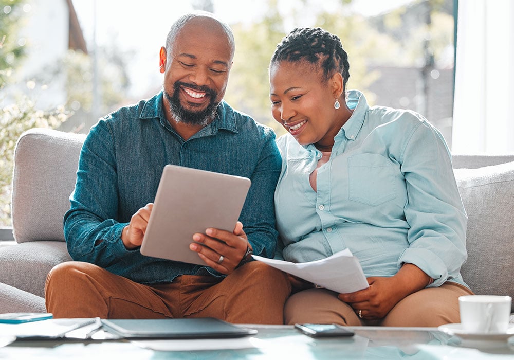 middle-aged-african-american-couple-smiling-and-looking-at-tablet-and-paperwork