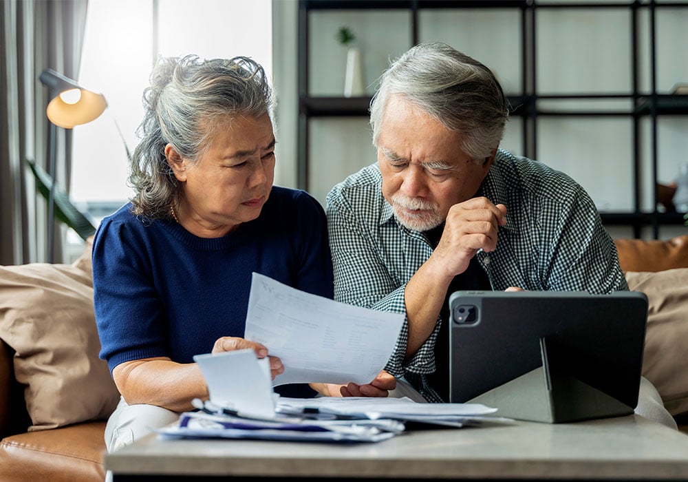 older-asian-couple-sitting-with-computer-and-paperwork-looking-contemplative