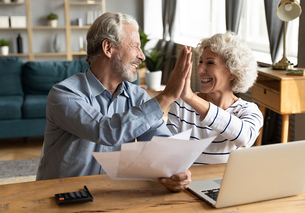 older-caucasian-couple-doing-a-high-five-by-their-laptop-and-calculator