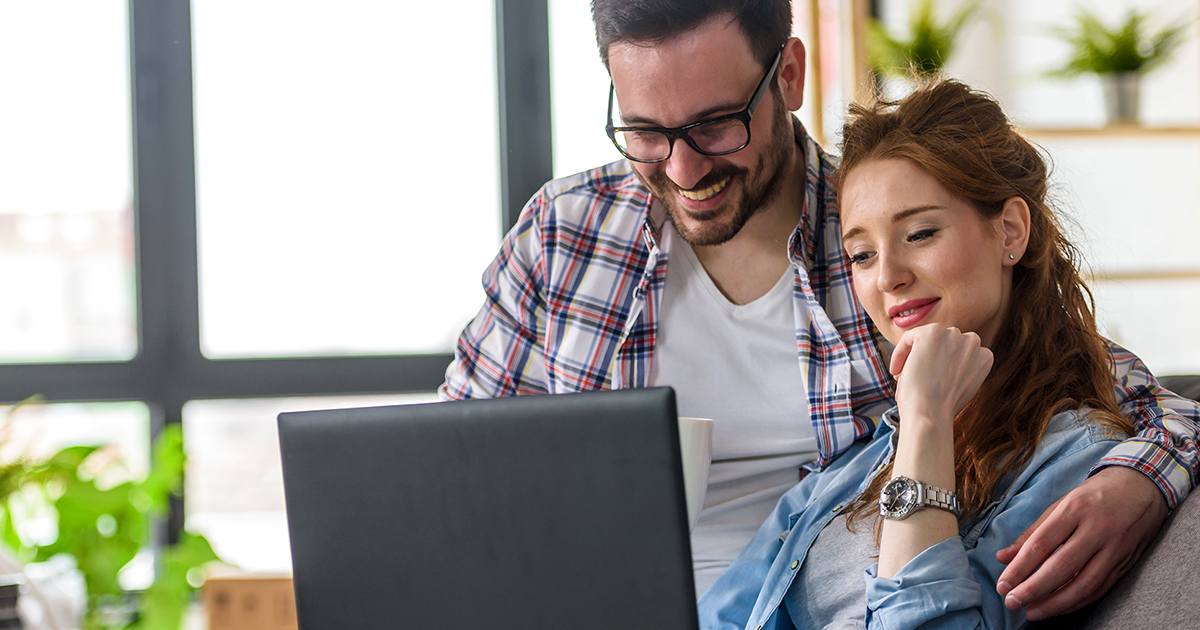 young couple smiling and looking at their laptop