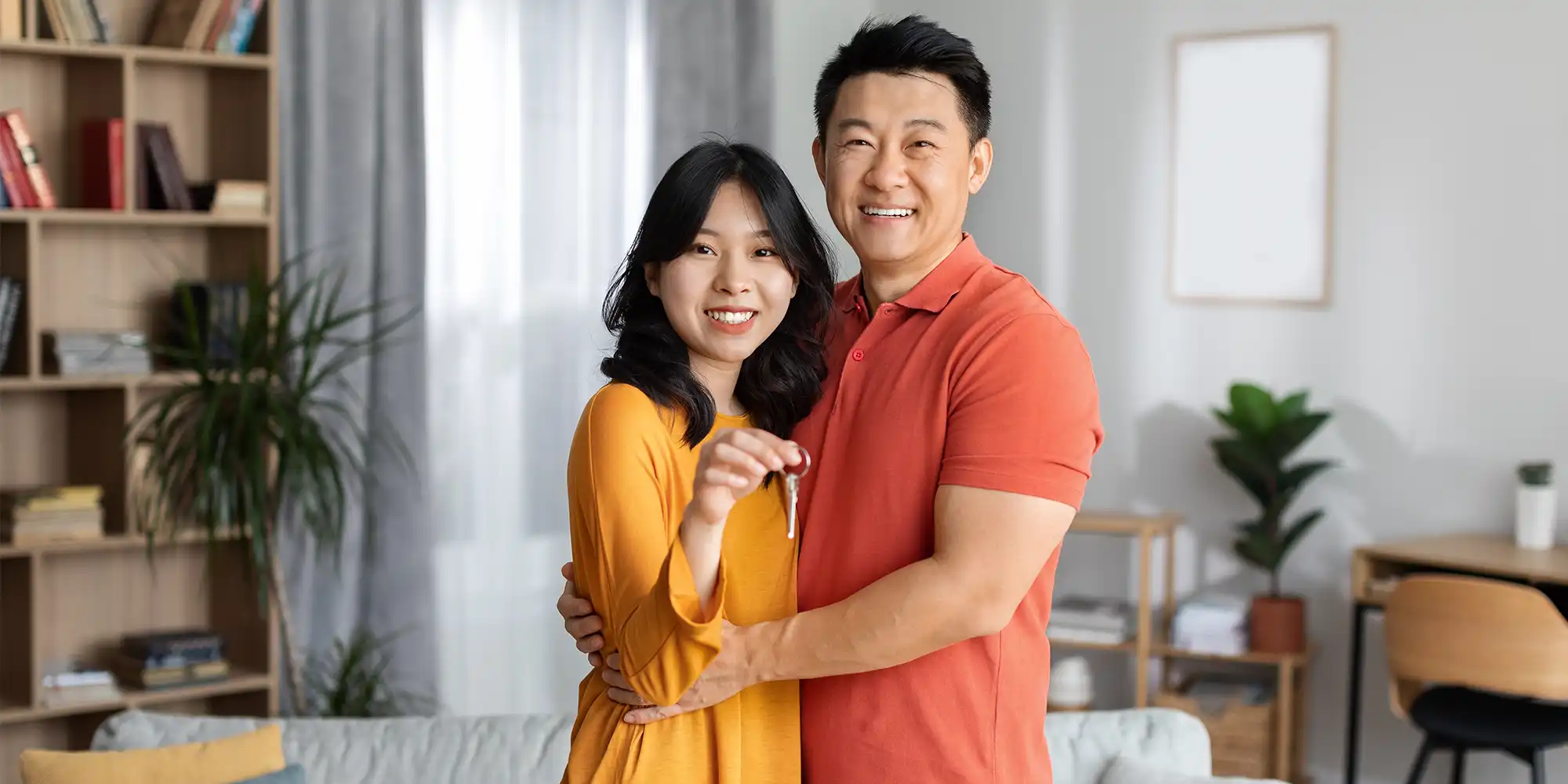young asian american couple standing in their modern livingroom holding their house key