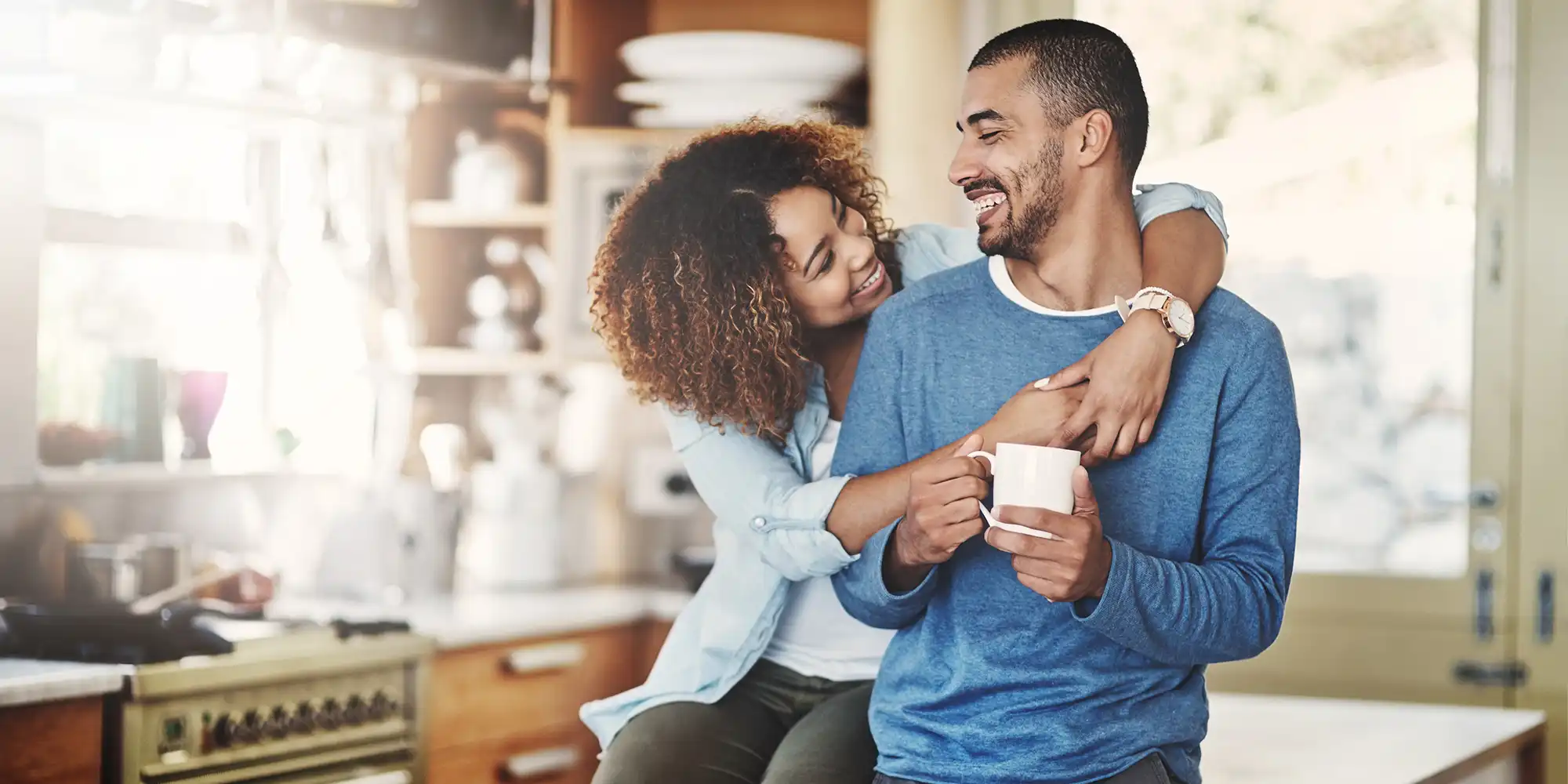 heterosexual BIPOC couple in their well lit kitchen having coffee while hugging