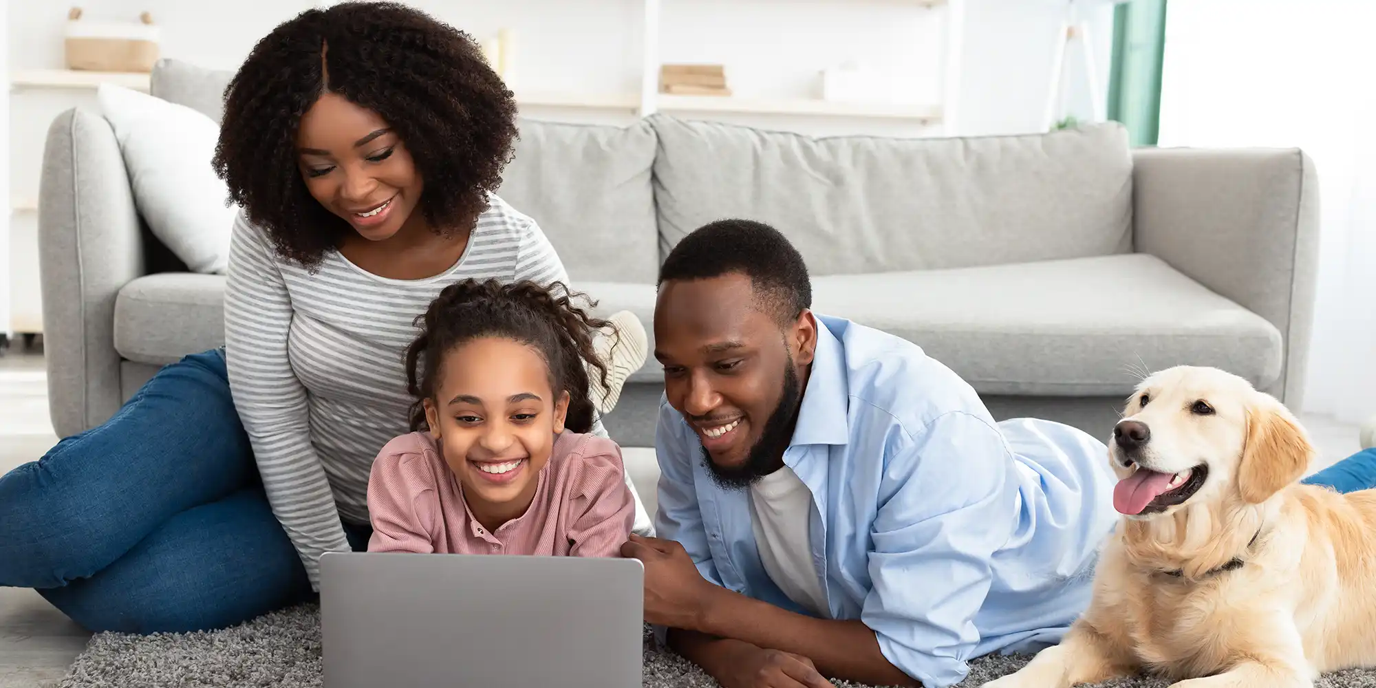 heterosexual BIPOC parents with young daughter using laptop on floor with golden lab dog
