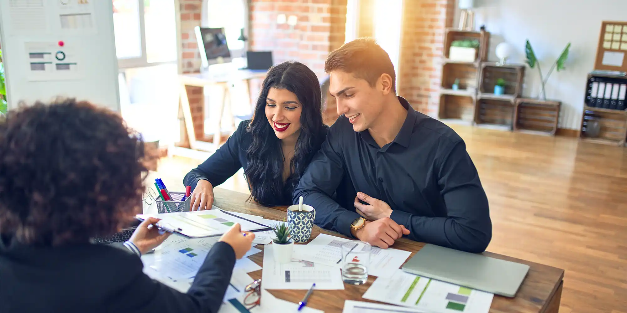 young BIPOC couple sitting at a loan officer's desk talking happily