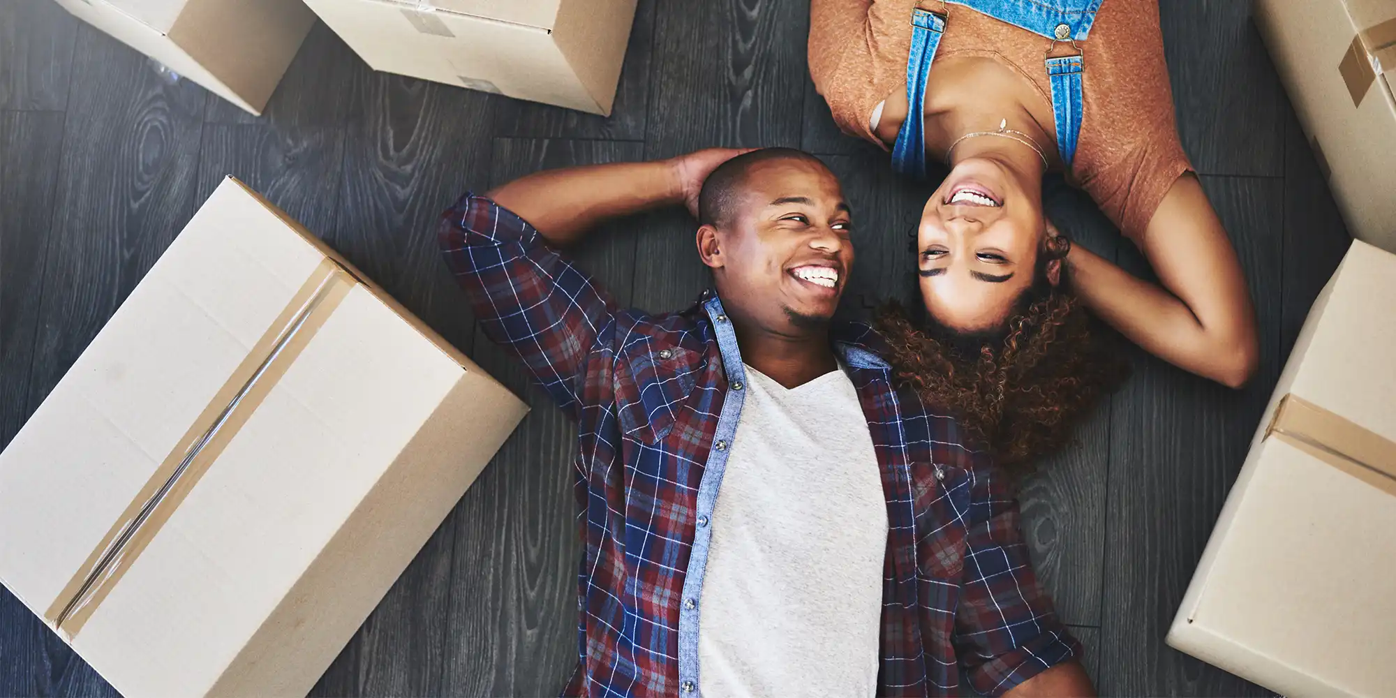 young adult african american heterosexual couple taking a rest on the floor smiling while surrounded by moving boxes