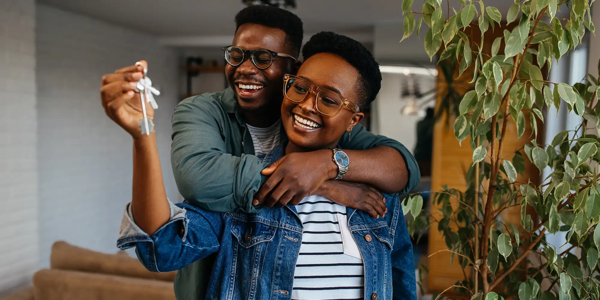happy african american couple holding their new house keys in their livingroom hugging