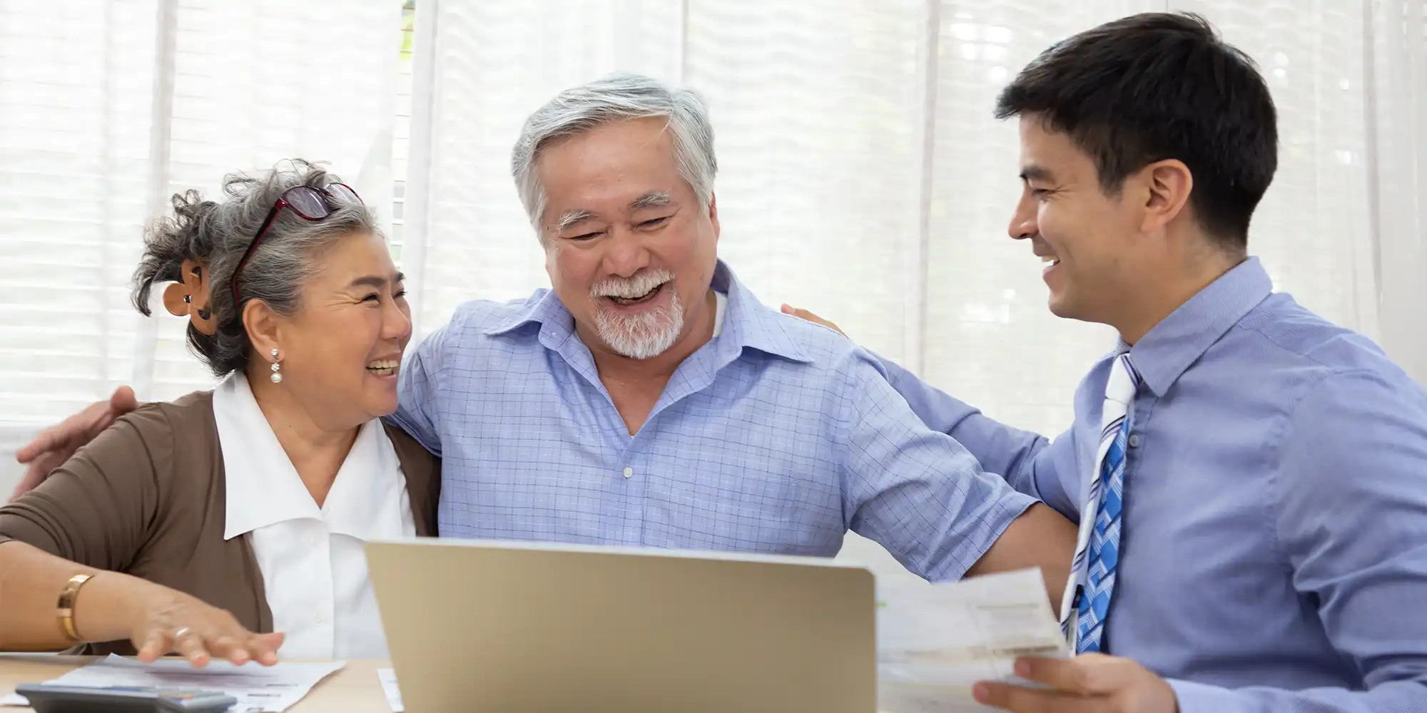 older asian american heterosexual couple sitting on a couch with a laptop and calculator meeting with young male loan officer with dark hair