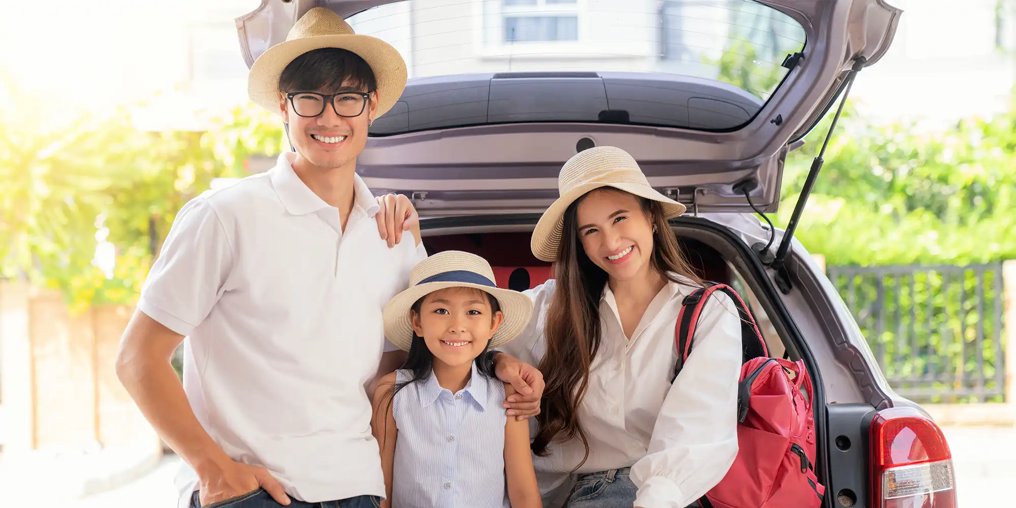 asian american couple and daughter sitting at back of grey vehicle packed for vacation