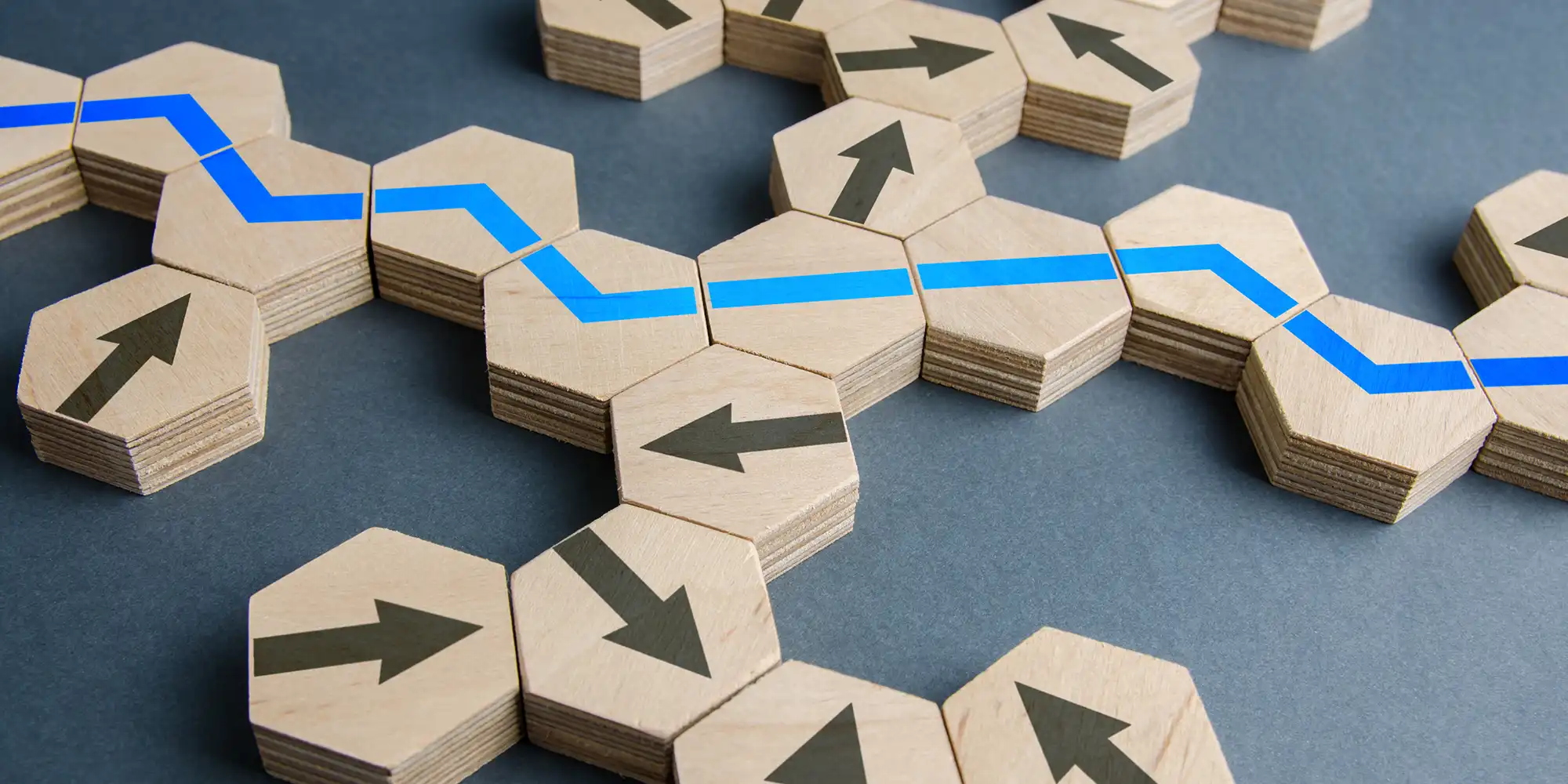 hexagonal wooden blocks making a path with blue line on top amongst other blocks with arrows pointing various directions
