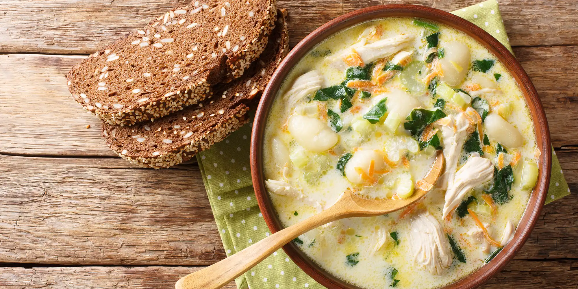 chicken gnocchi soup in dark bowl sitting next to two slices of pumpernickel bread on wooden table