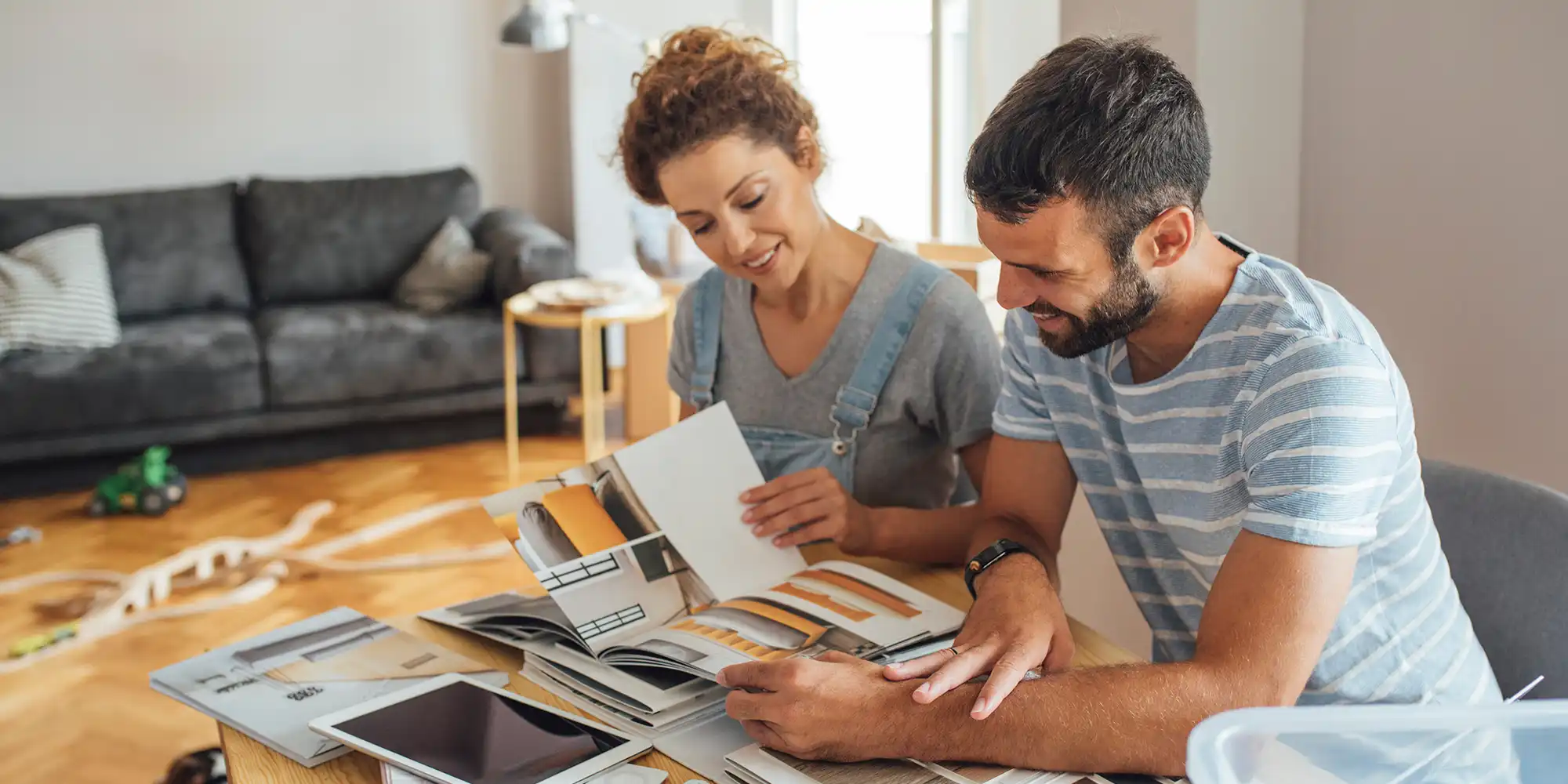 caucasian heterosexual couple sitting at kitchen table with books and tablet planning home renovation