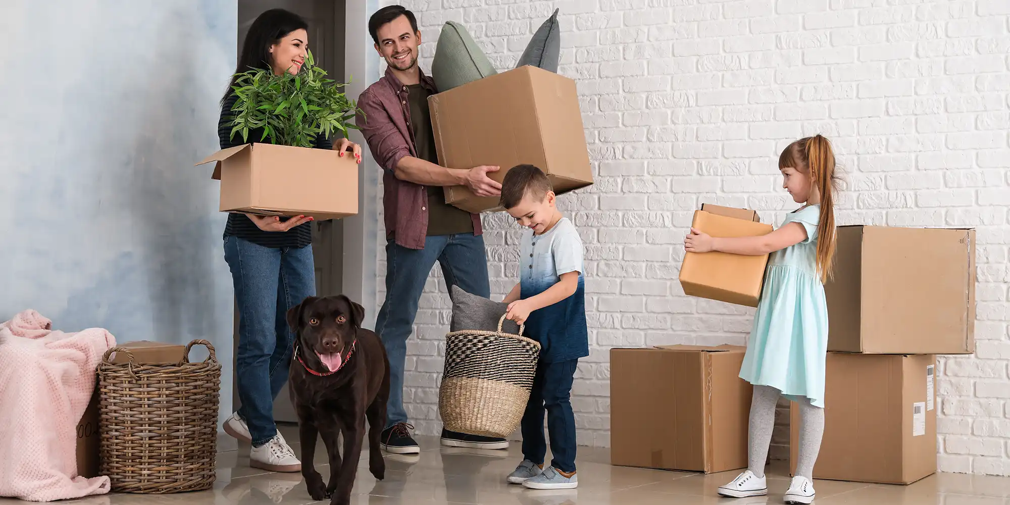 caucasian parents with son and daughter and a chocolate lab holding their belongings in boxes while standing in new home