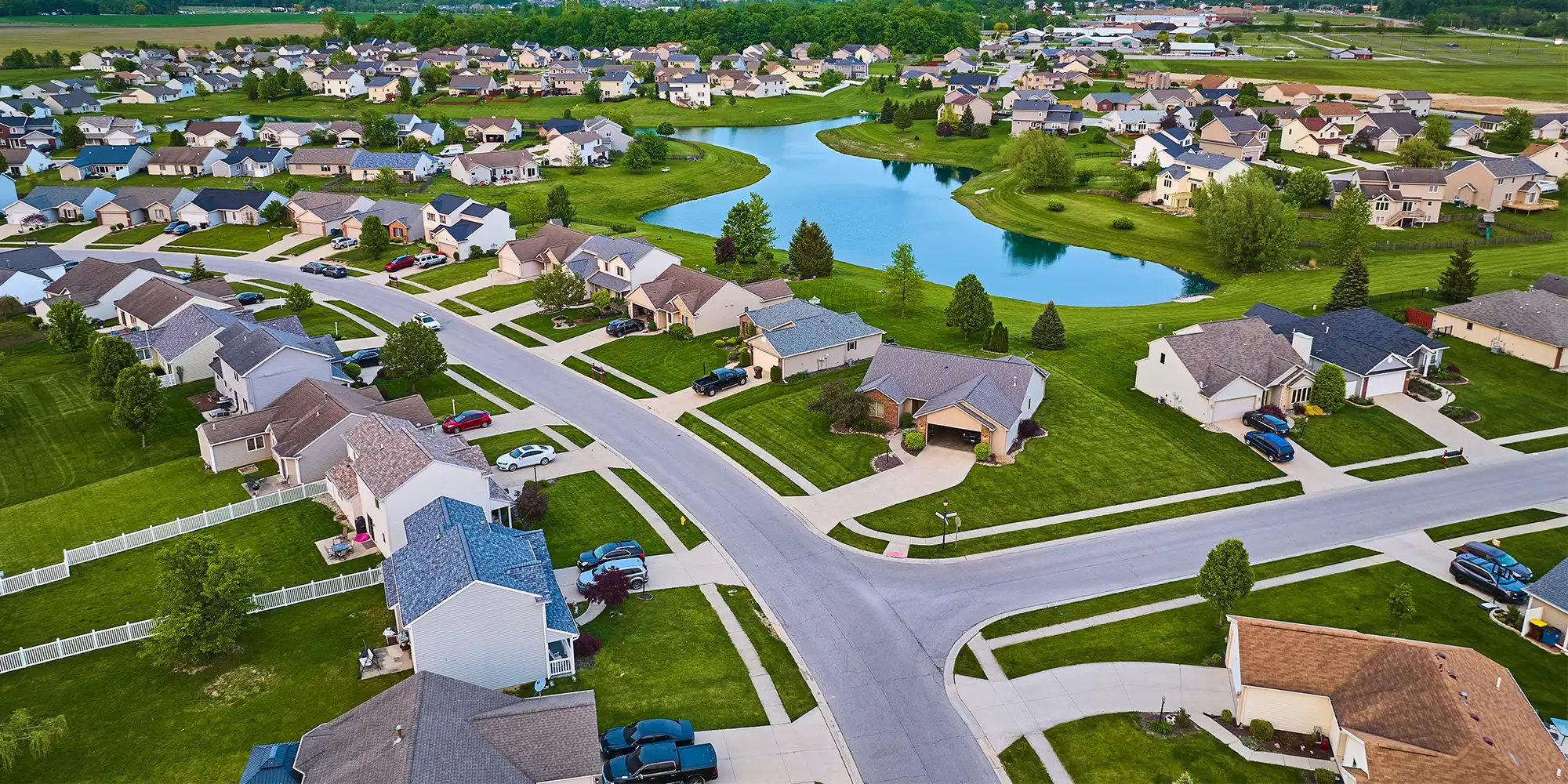 aerial view of a well maintained suburban neighborhood full of green grass and a pond behind homes