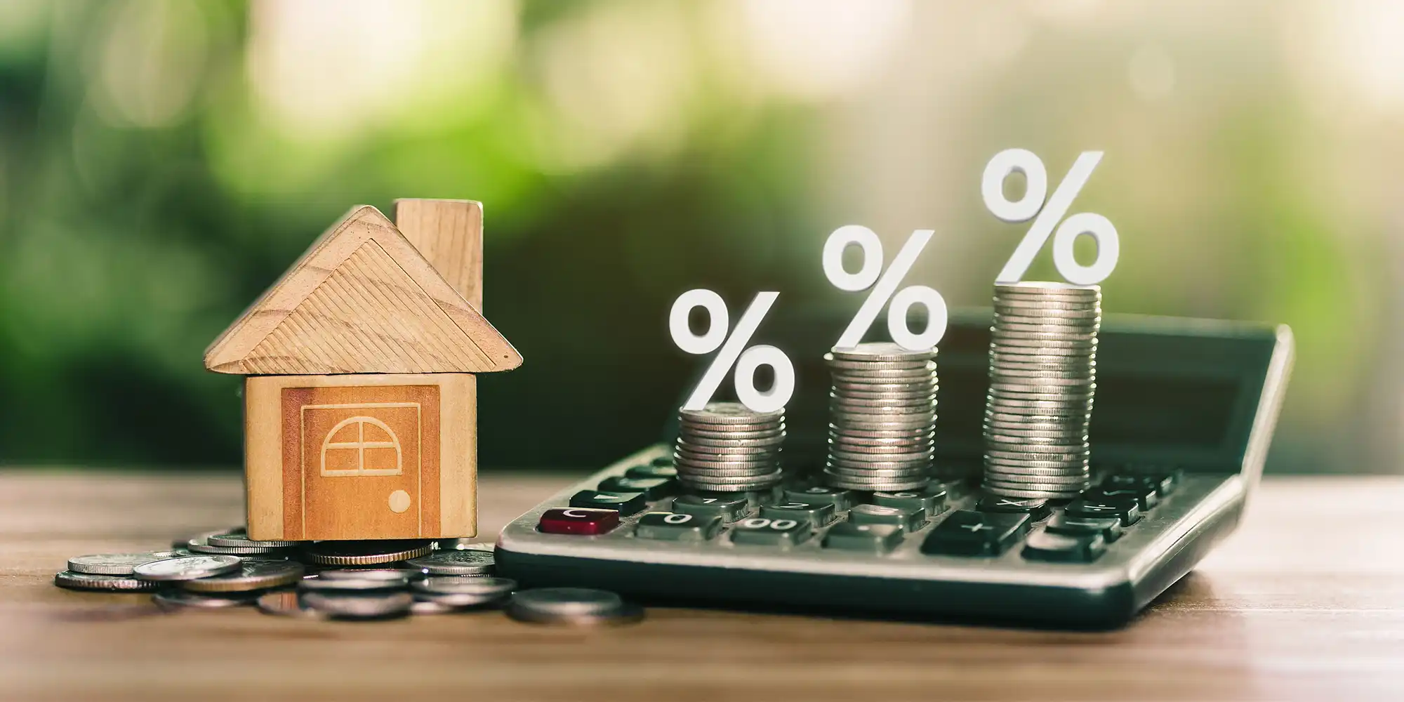 small wooden home next to calculator and coin stacks with percentage signs on top
