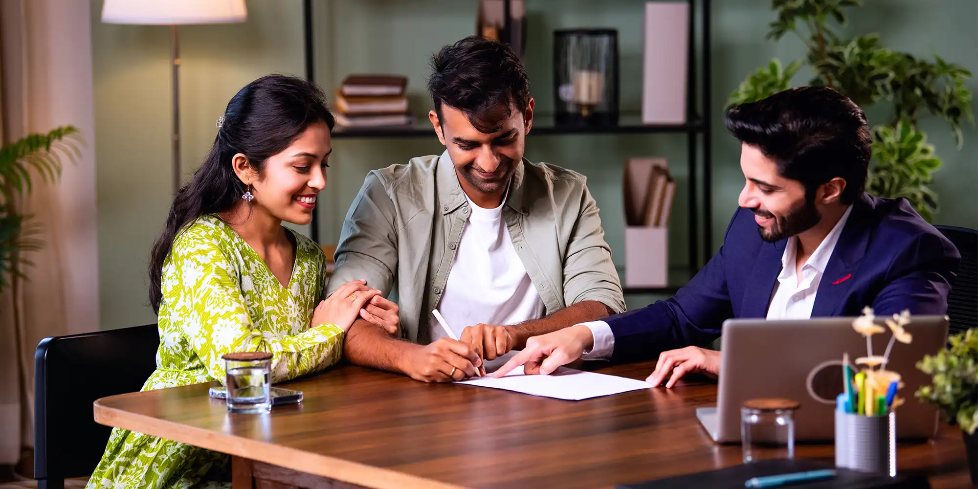 indian asian american couple signing loan papers with indian asian american loan officer at a mahogany desk
