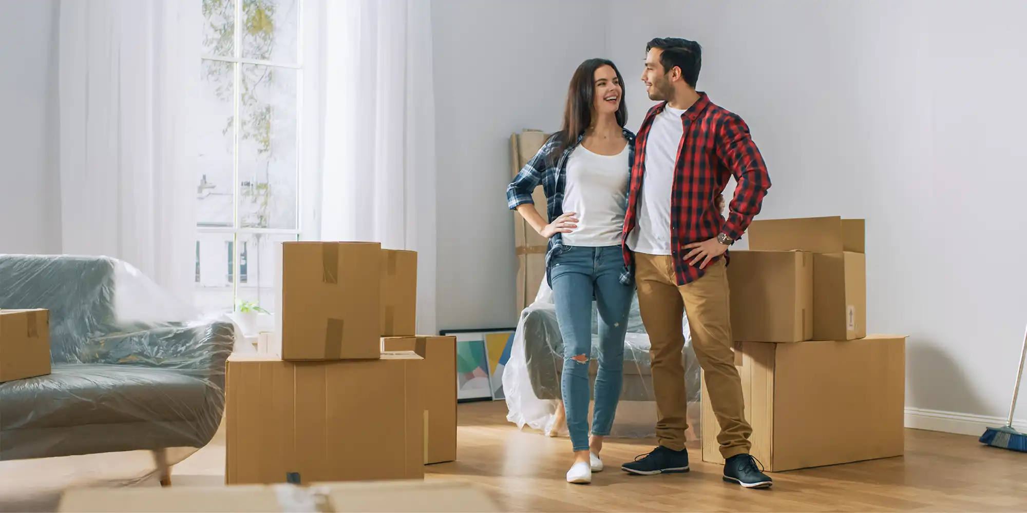 young couple standing in light living room surrounded by moving boxes