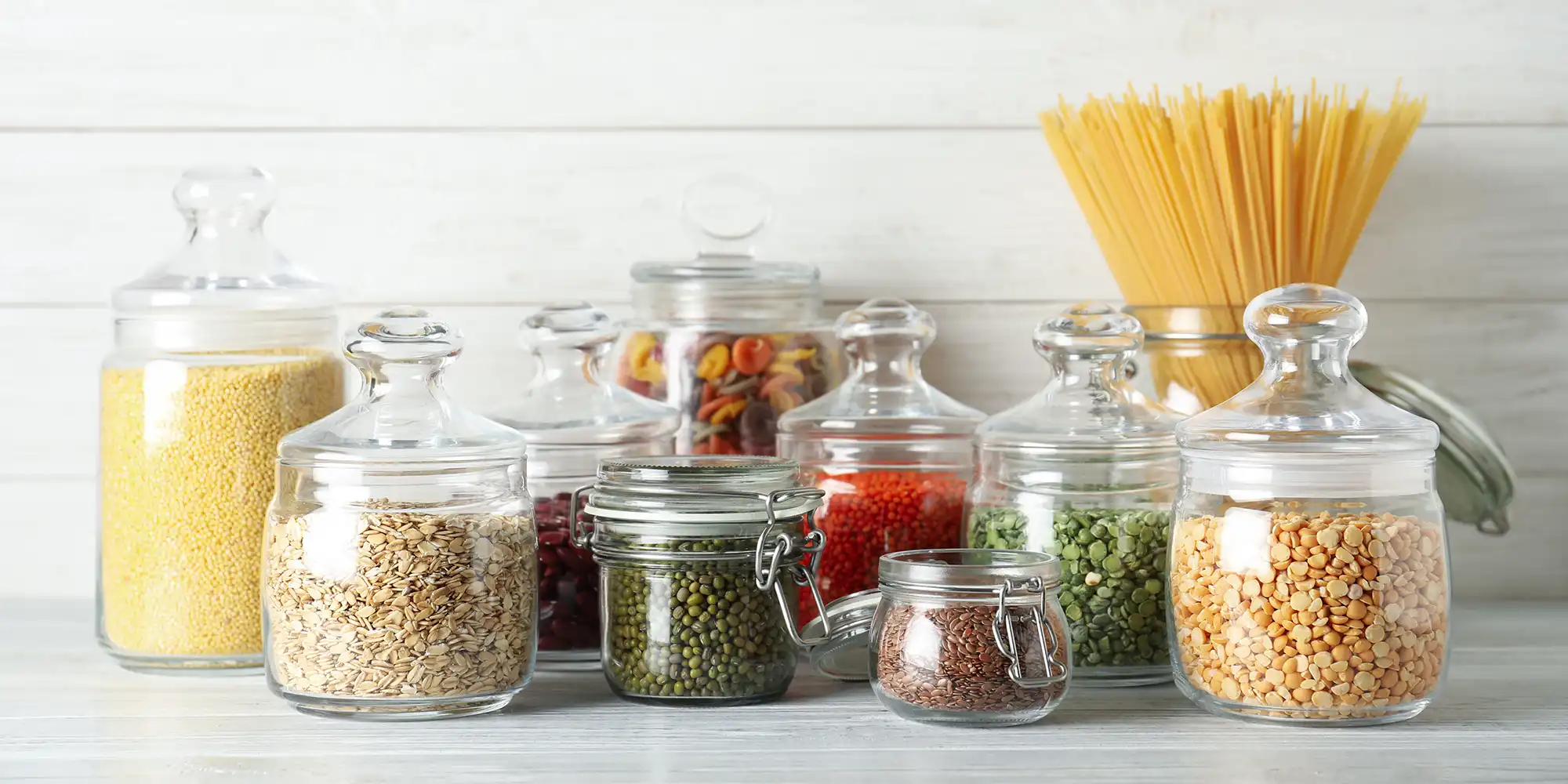 dry pantry goods in stylish glass jars in front of pale wooden background