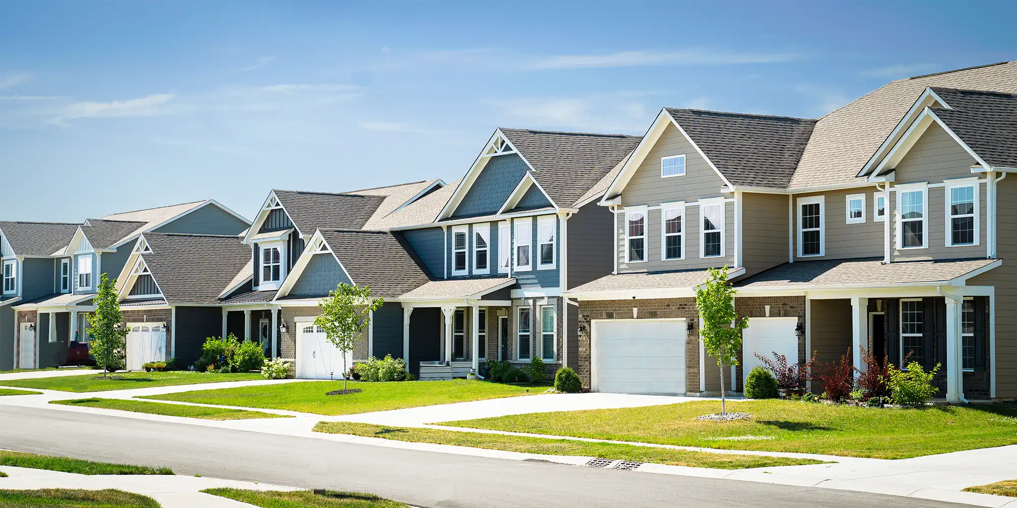 suburban block of two story homes with garages and green lawns on a sunny day