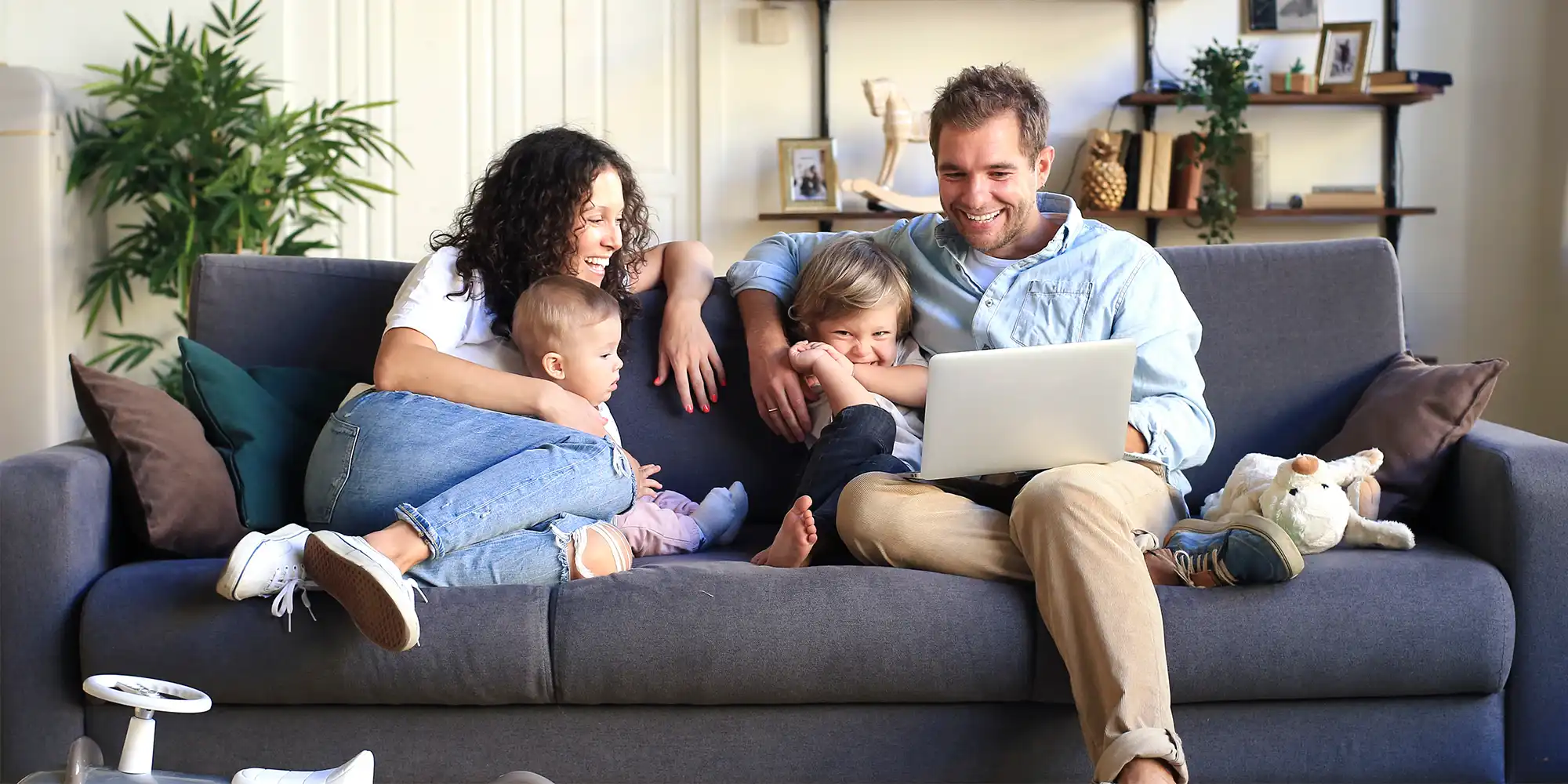 young caucasian family sitting on dark grey sofa looking at a laptop and smiling