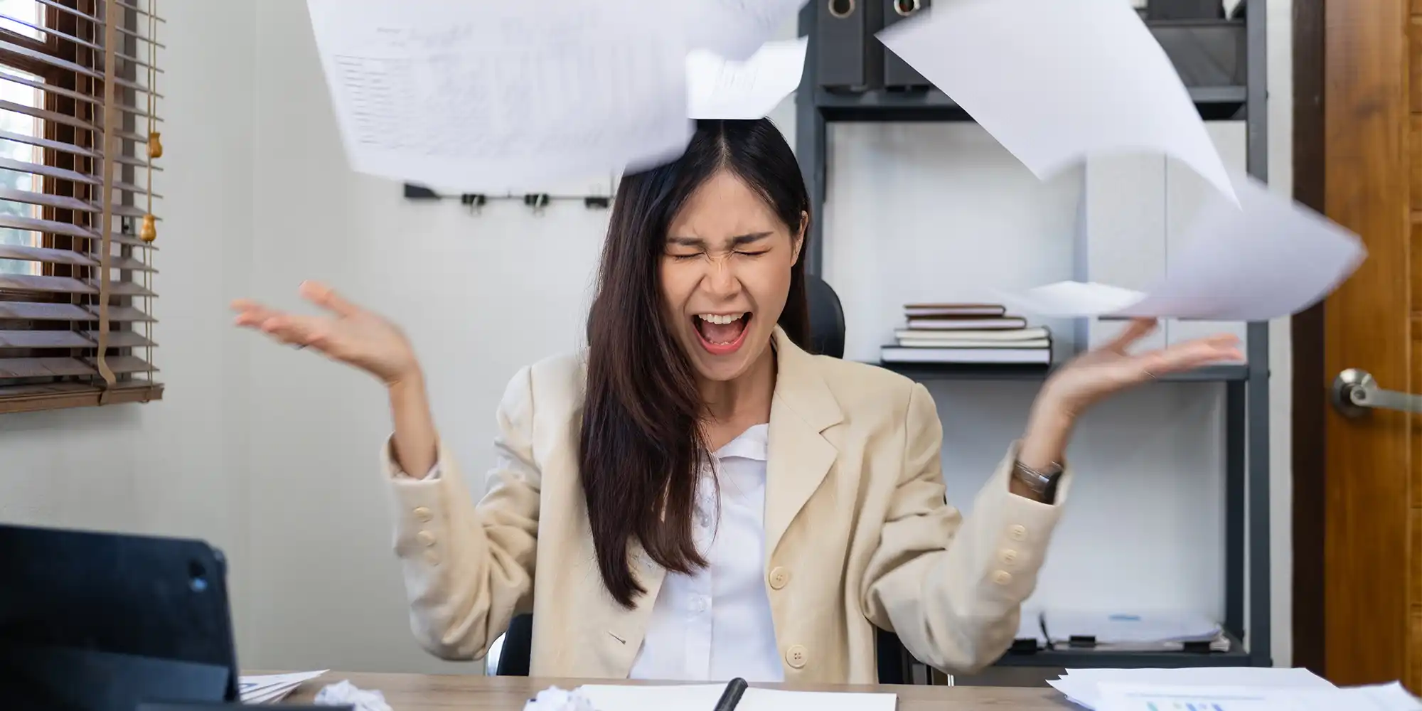 asian american young woman throwing papers up into the air while at her desk