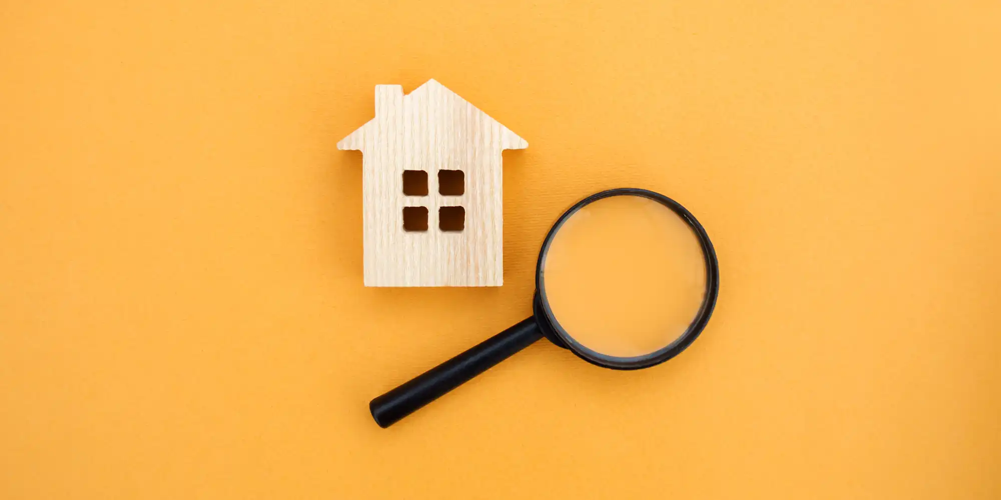 wooden block home shape next to magnifying glass on sunny yellow surface