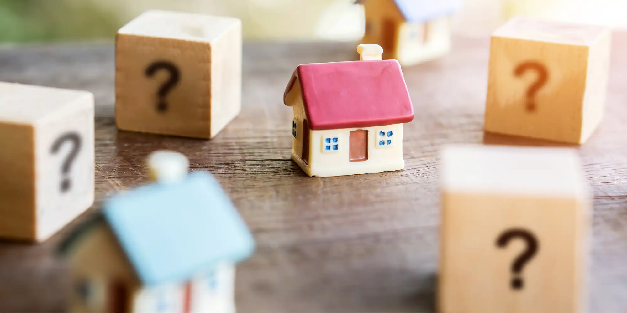 miniature wooden block house with red roof surrounded by mini wooden blocks with question marks on them