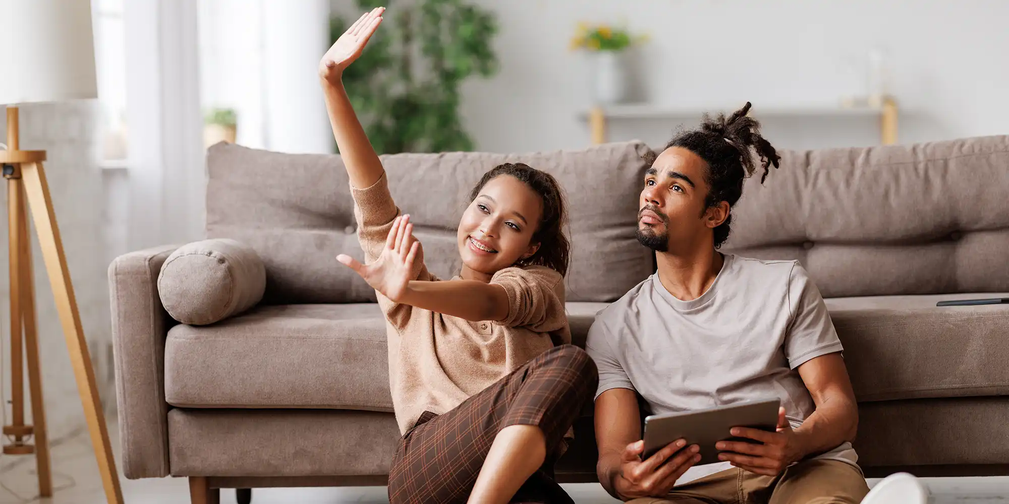 young african american couple sitting on the floor in front of their couch motioning with their hands indicating they're thinking of redecorating