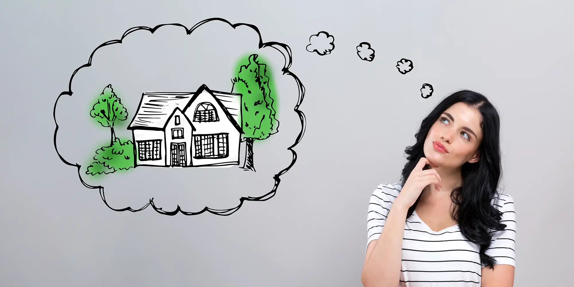 young caucasian woman with long dark brown hair standing in front of grey wall thinking with a thought bubble illustration by her with a house and trees in it