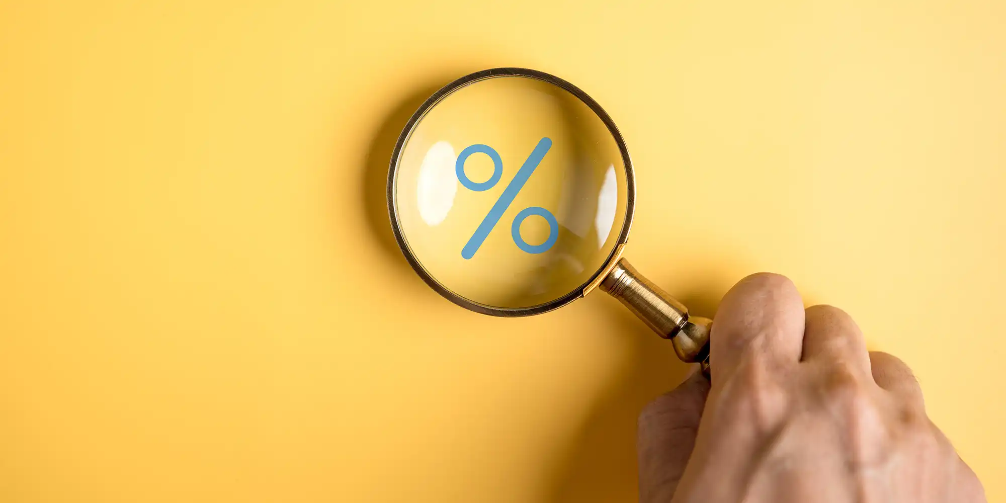 male hand holding a magnifying glass over a percentage sign on a yellow background