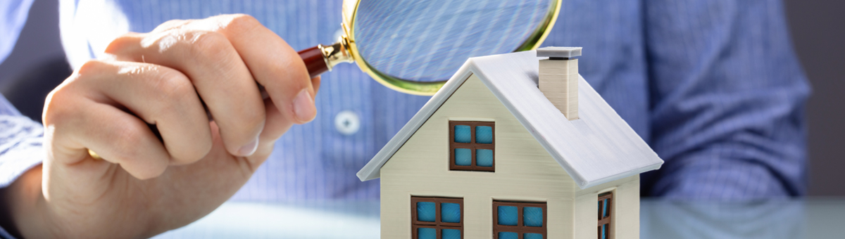 person wearing light blue shirt holding magnifying glass looking at miniature home