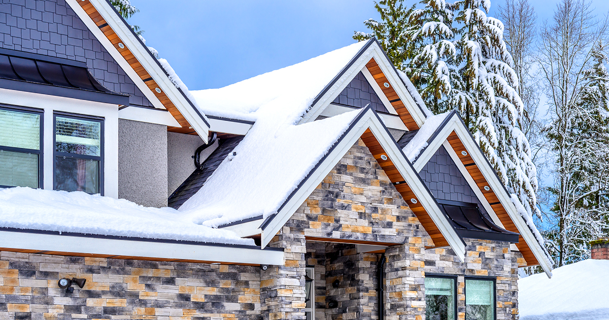 brick home with multiple snow covered pitches on roof