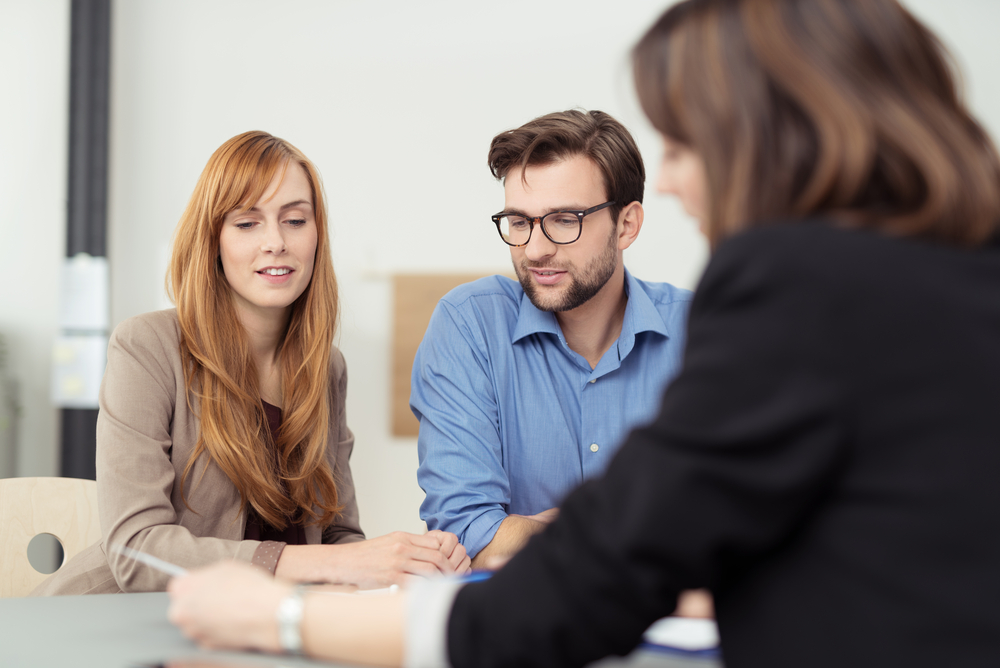 woman with long red hair and man wearing glasses sit at a desk with their female loan officer