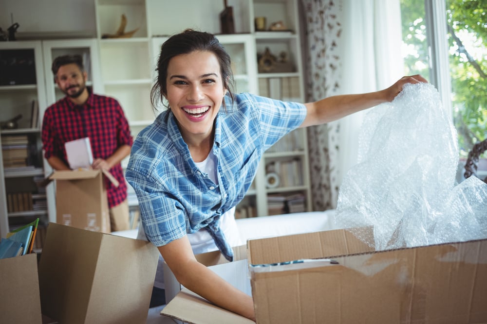 woman unpacking a box smiling with man in the background holding a box