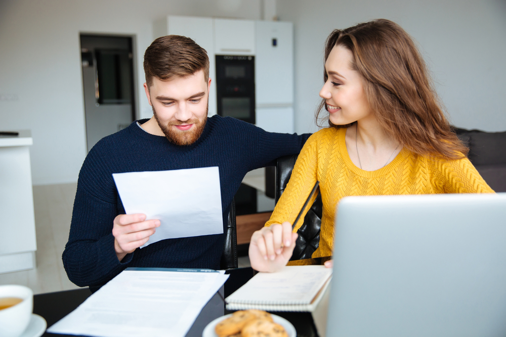 white couple looking at paperwork while sitting at a desk with a laptop