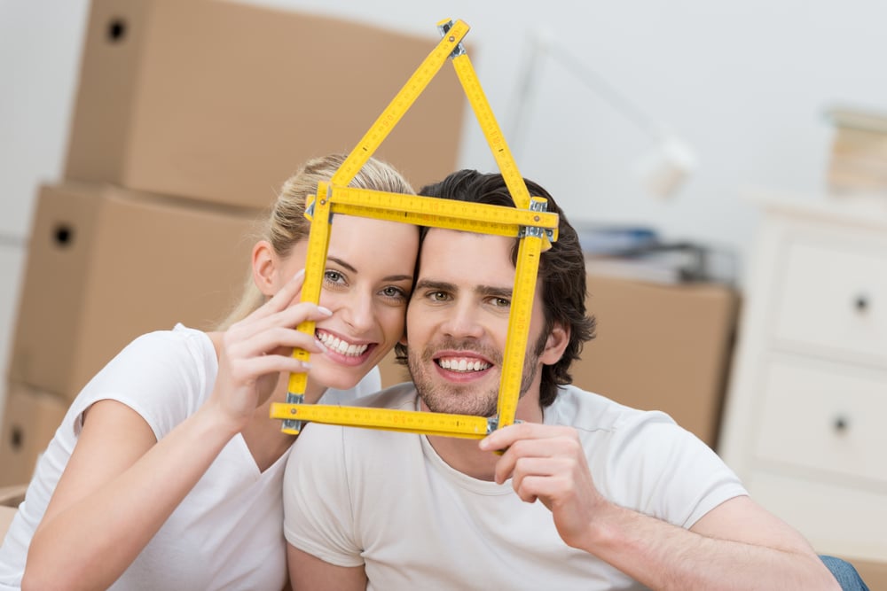 white couple wearing white shirts holding a yellow house-like item in front of them