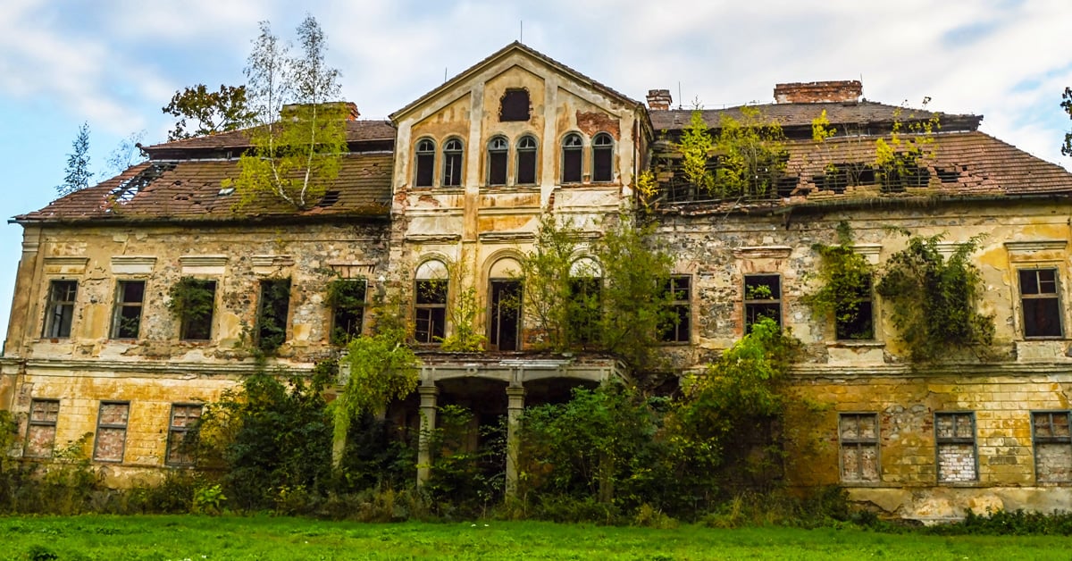 Older three-story building that is overgrown with foliage