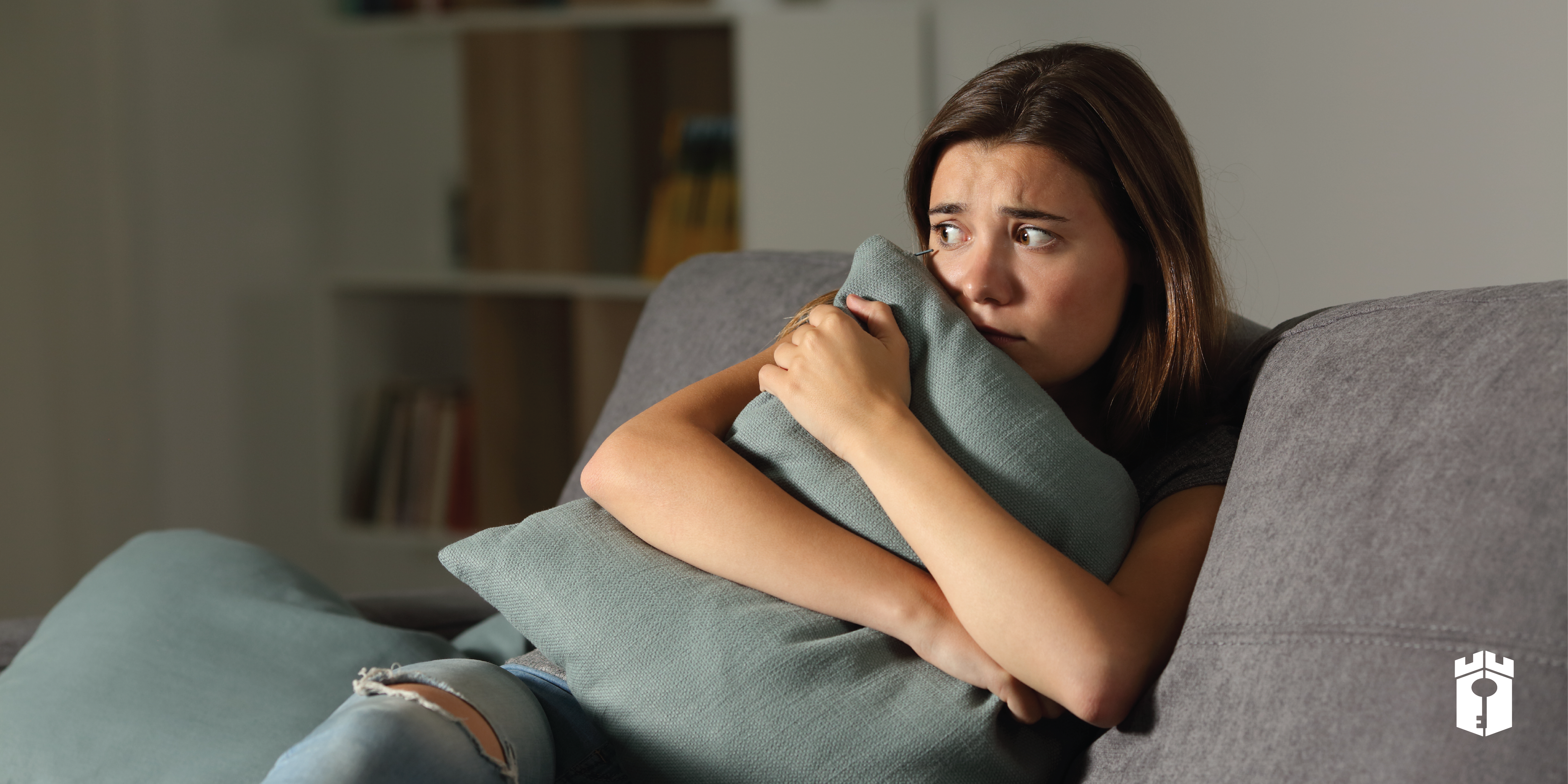 woman scared clutching pillow while sitting on couch