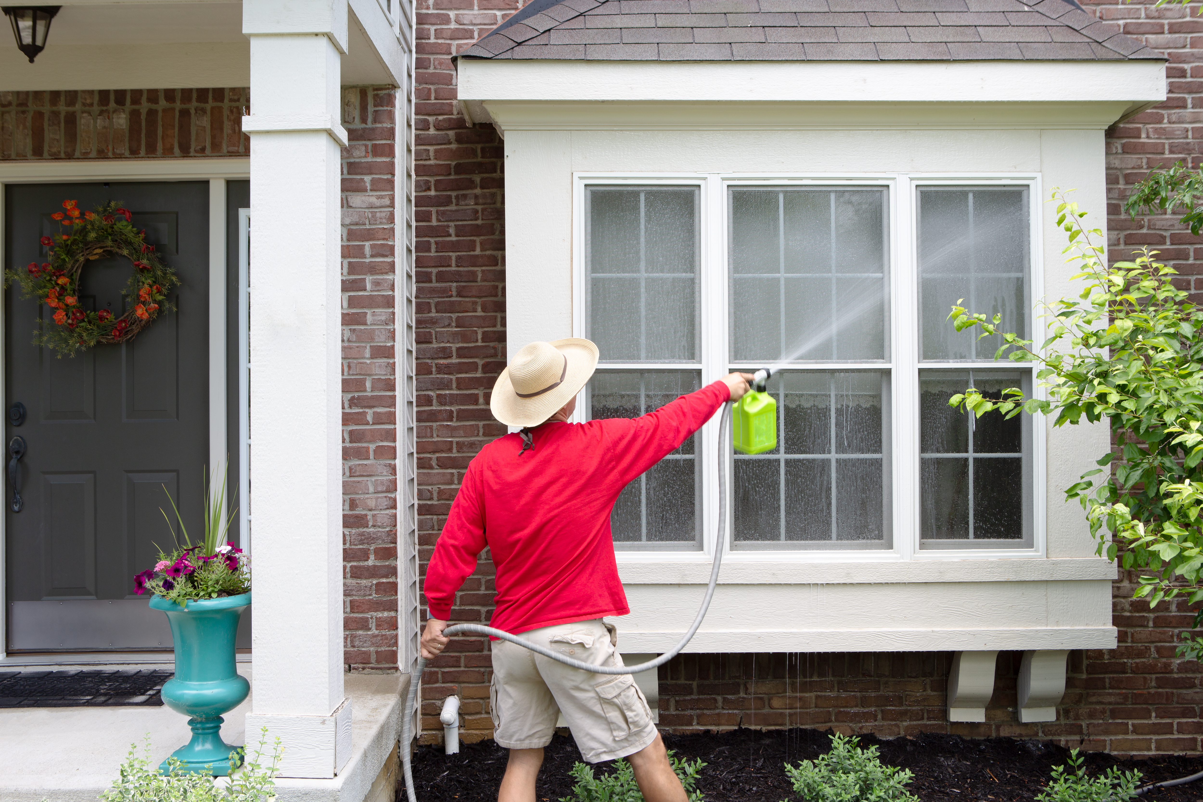 woman washing windows outside with garden hose