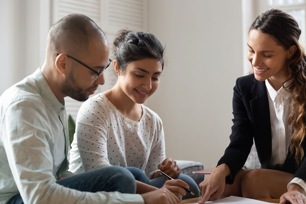 BIPOC couple wearing light-colored shirts smiling and looking over documents with their smiling female loan officer